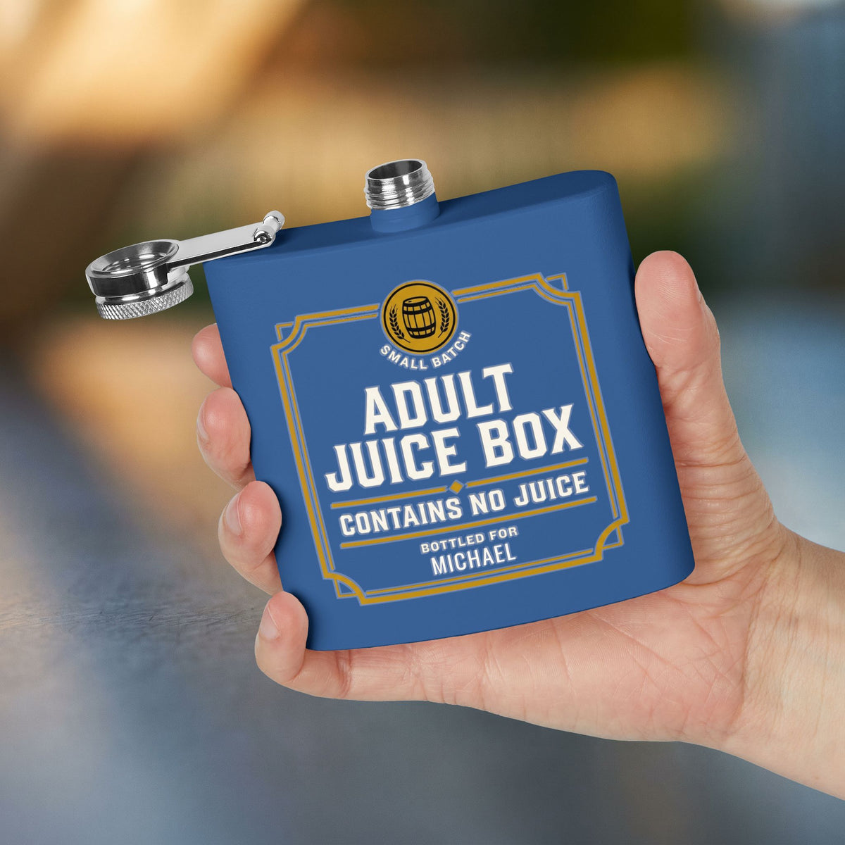 A hand holds a royal blue Humorous Flask, personalized with "Michael", with the cap open and visible