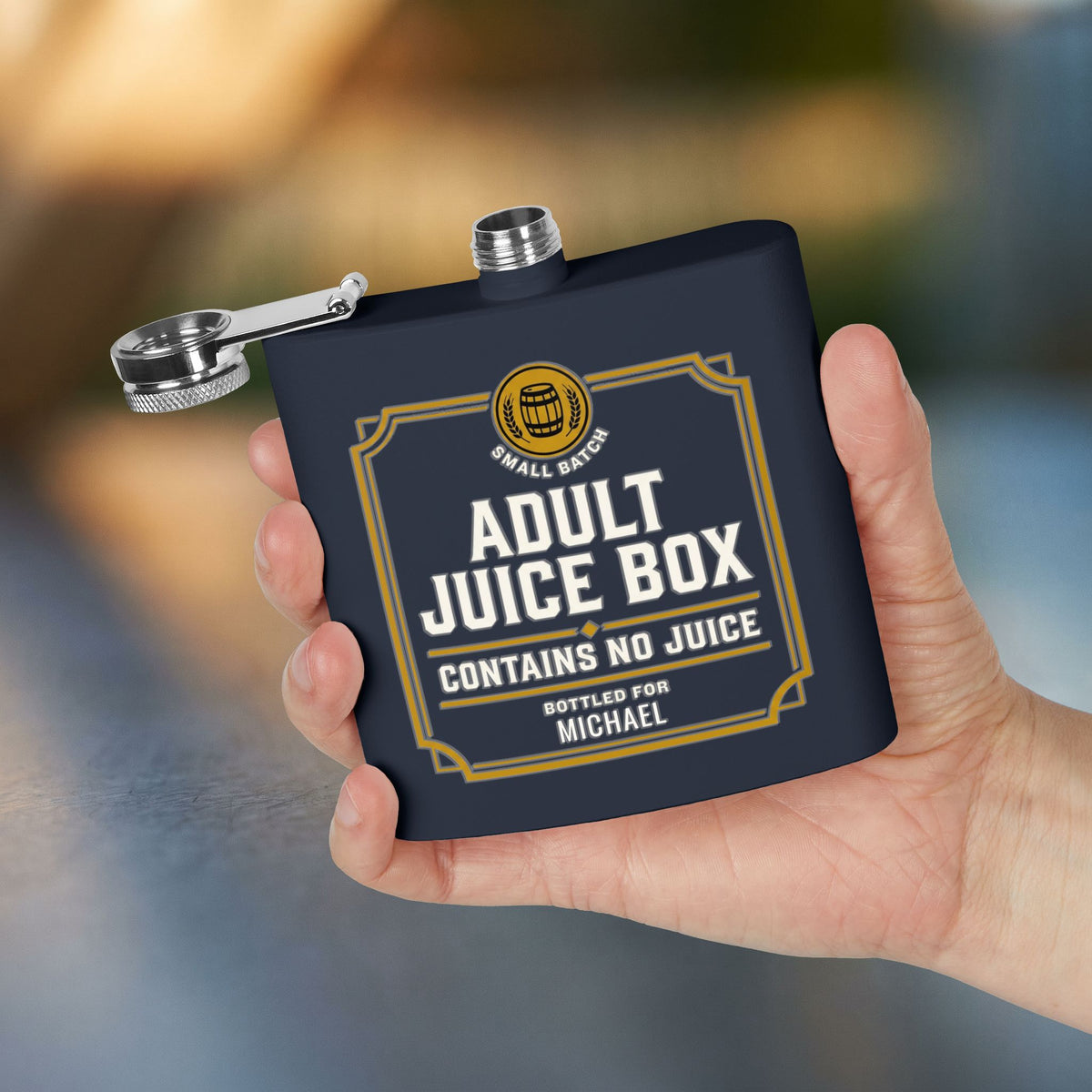 A hand holds a navy blue Humorous Flask, personalized with "Michael", with the cap open and visible