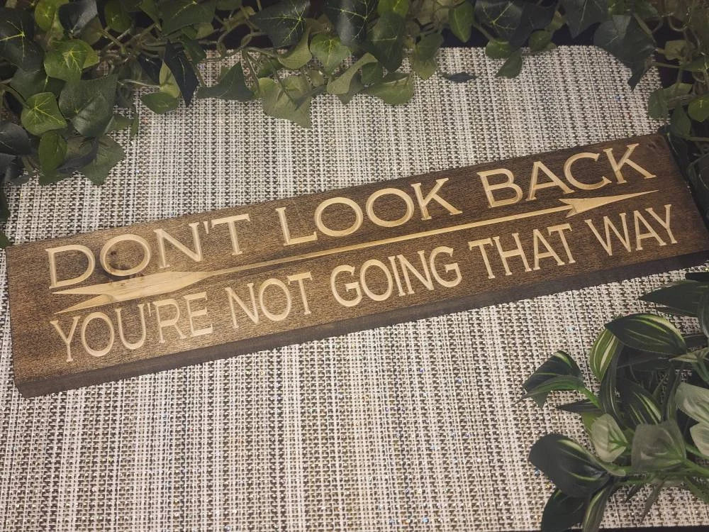 "Don't Look Back, You're Not Going That Way" wooden sign displayed as motivational wall art in a home office.