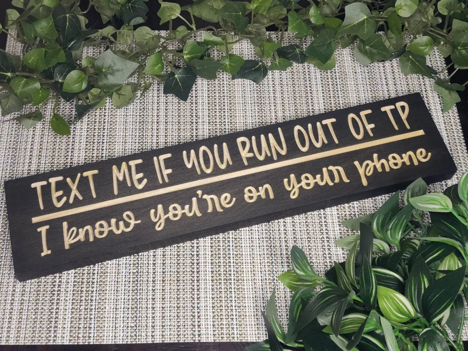 Rustic wooden bathroom sign reading Text Me if You Run Out of TP - I Know You're on Your Phone displayed in a modern guest bathroom.