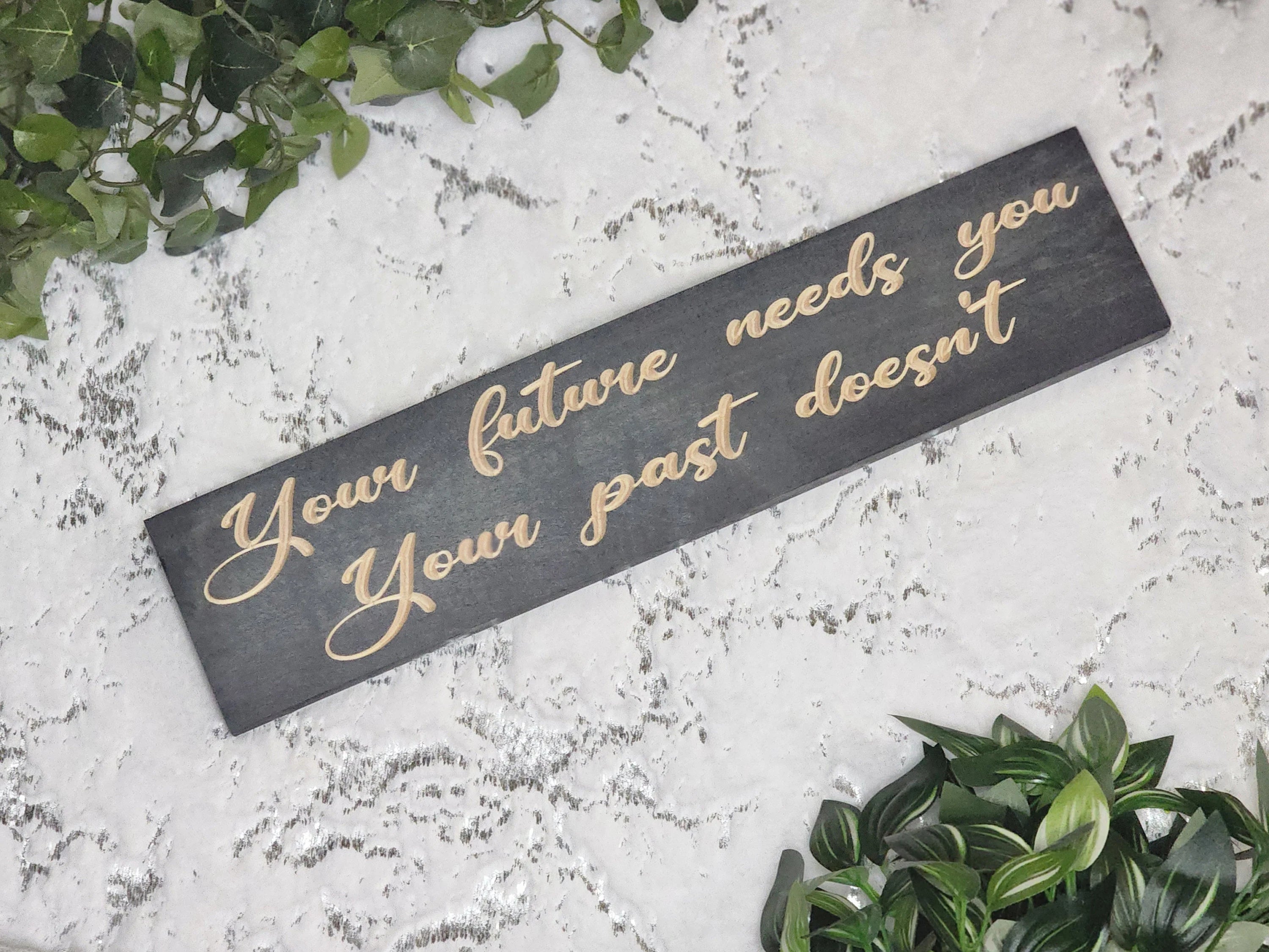 Wooden quote sign reading Your Future Needs You, Your Past Doesn't in a motivational home office.