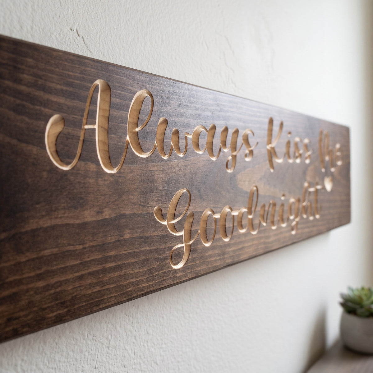 Close-up of the carved letters on the Always Kiss Me Goodnight sign, natural pine inside the cuts against the stained grain