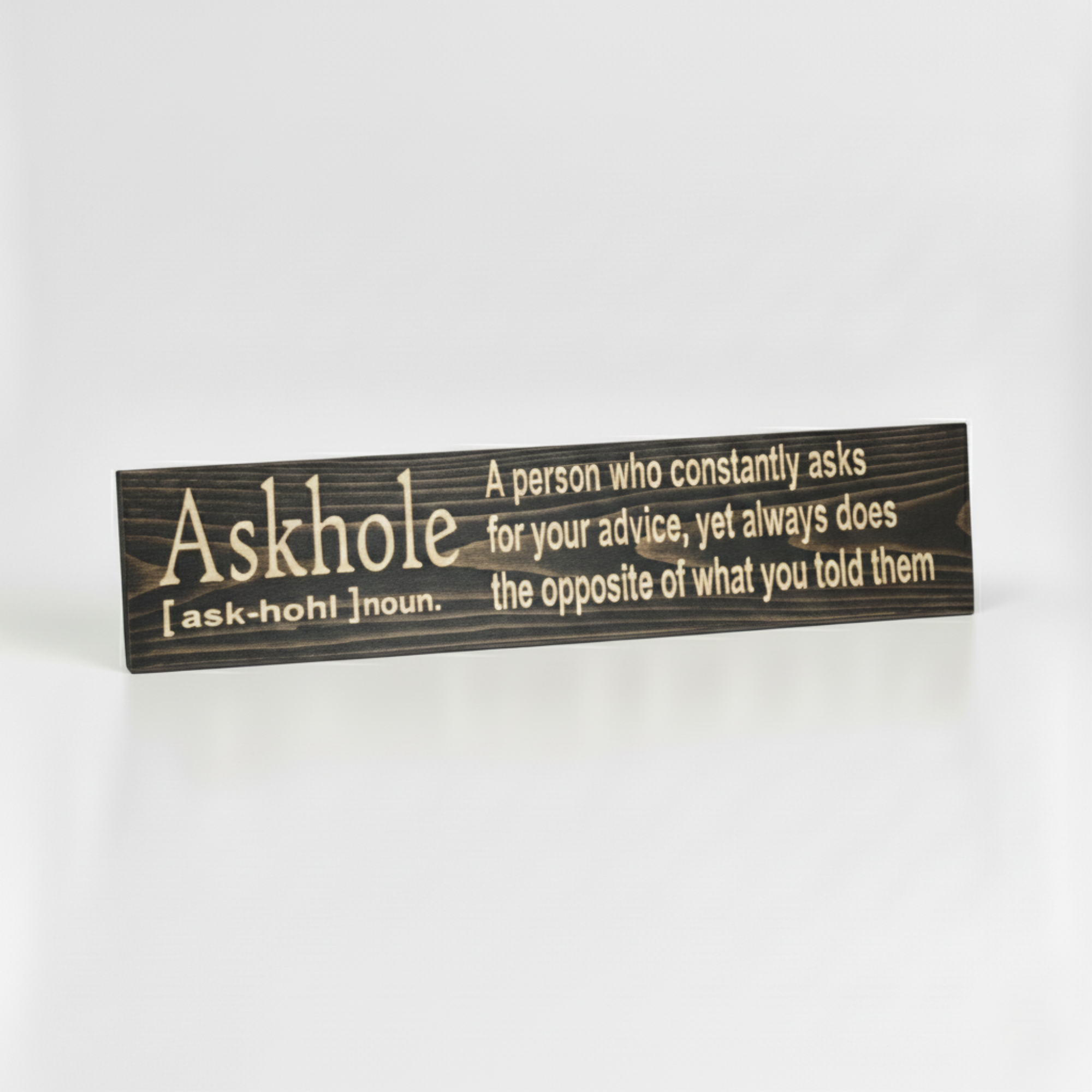 Angled view of the handcrafted Askhole definition wood sign, showing the high-contrast natural wood grain against a dark finish.
