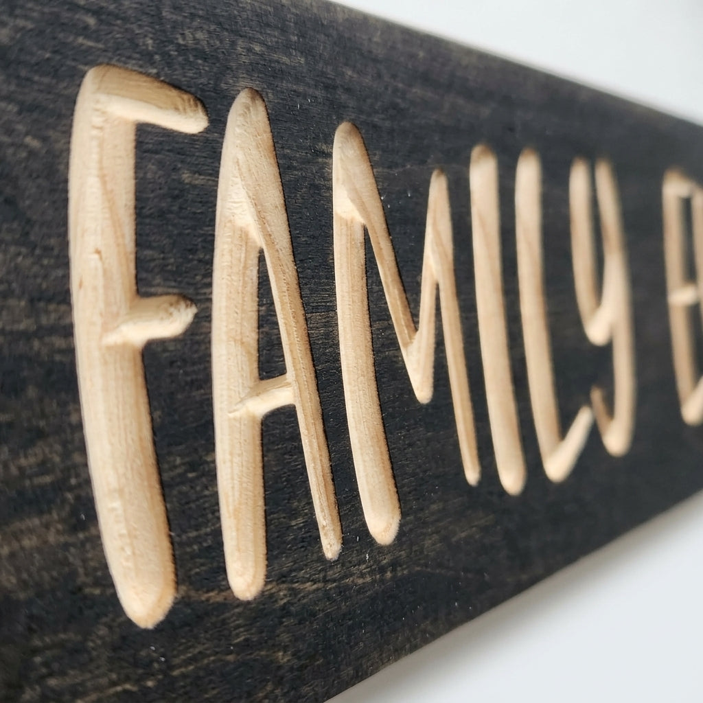 A close-up, angled view of the Best Family Ever Sign shows the deep carving of the letters into the dark wood
