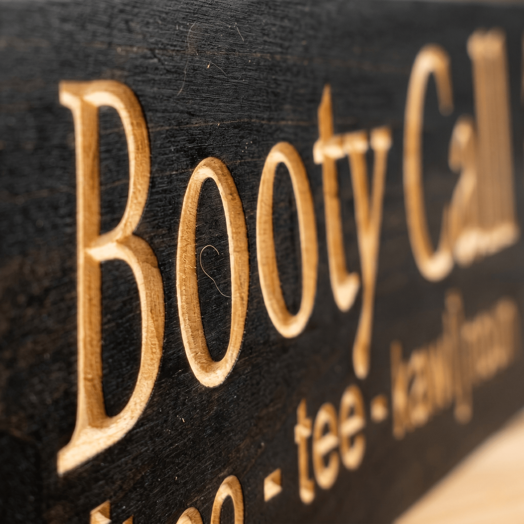 Close-up macro of deeply CNC-carved Booty Call lettering on solid wood showing dimensional 2.5D routing detail and natural grain through Ebony stain