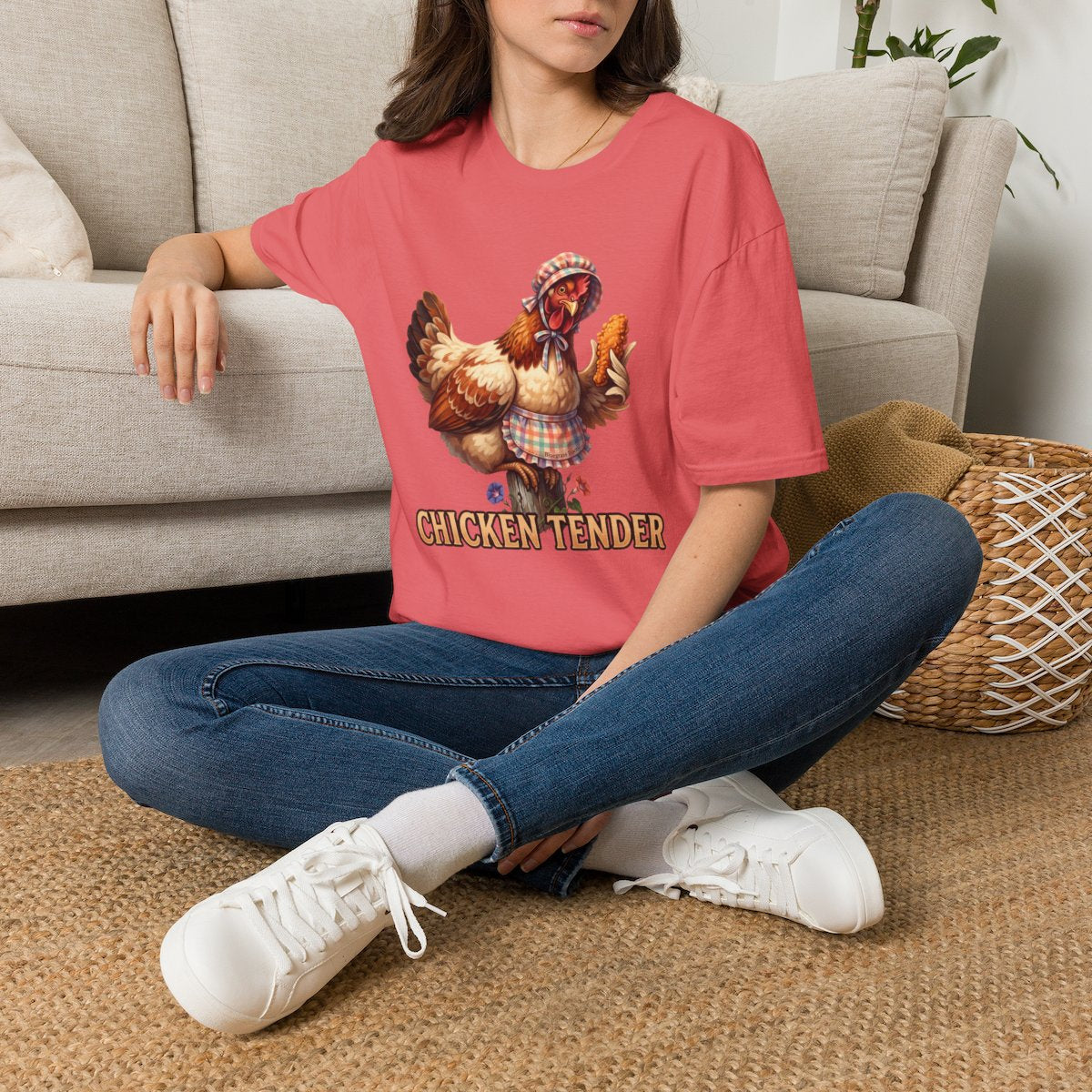 A woman sits cross-legged on a woven rug, wearing an oversized coral pink Chicken T Shirt - Chicken Tender