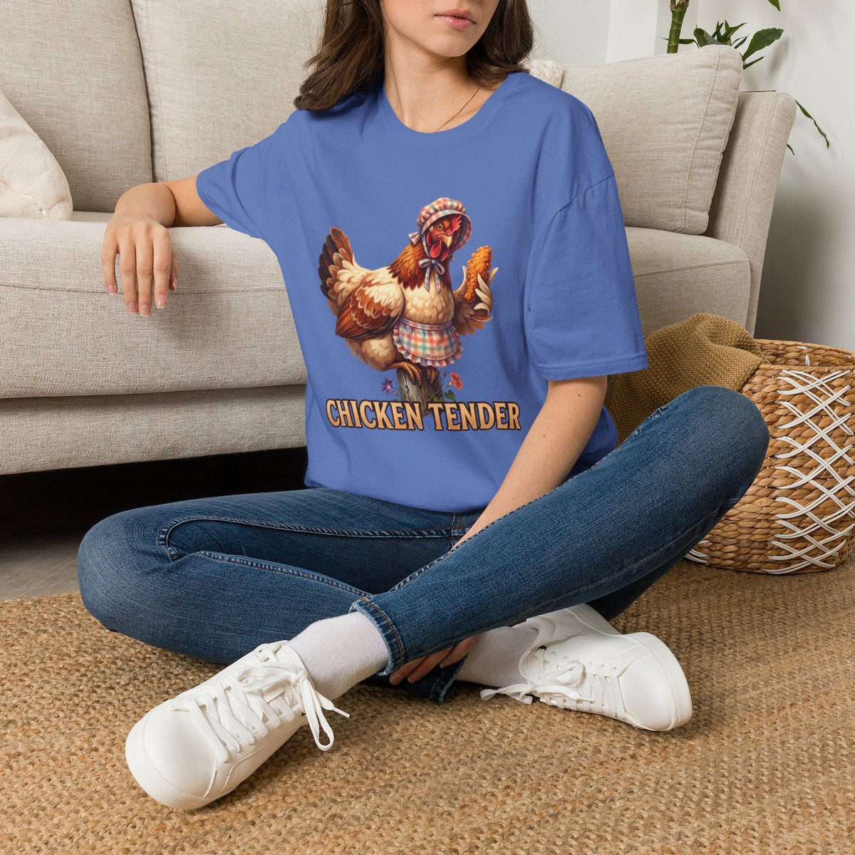 A woman sits cross-legged on a rug, wearing an oversized blue Chicken T Shirt - Chicken Tender, looking down