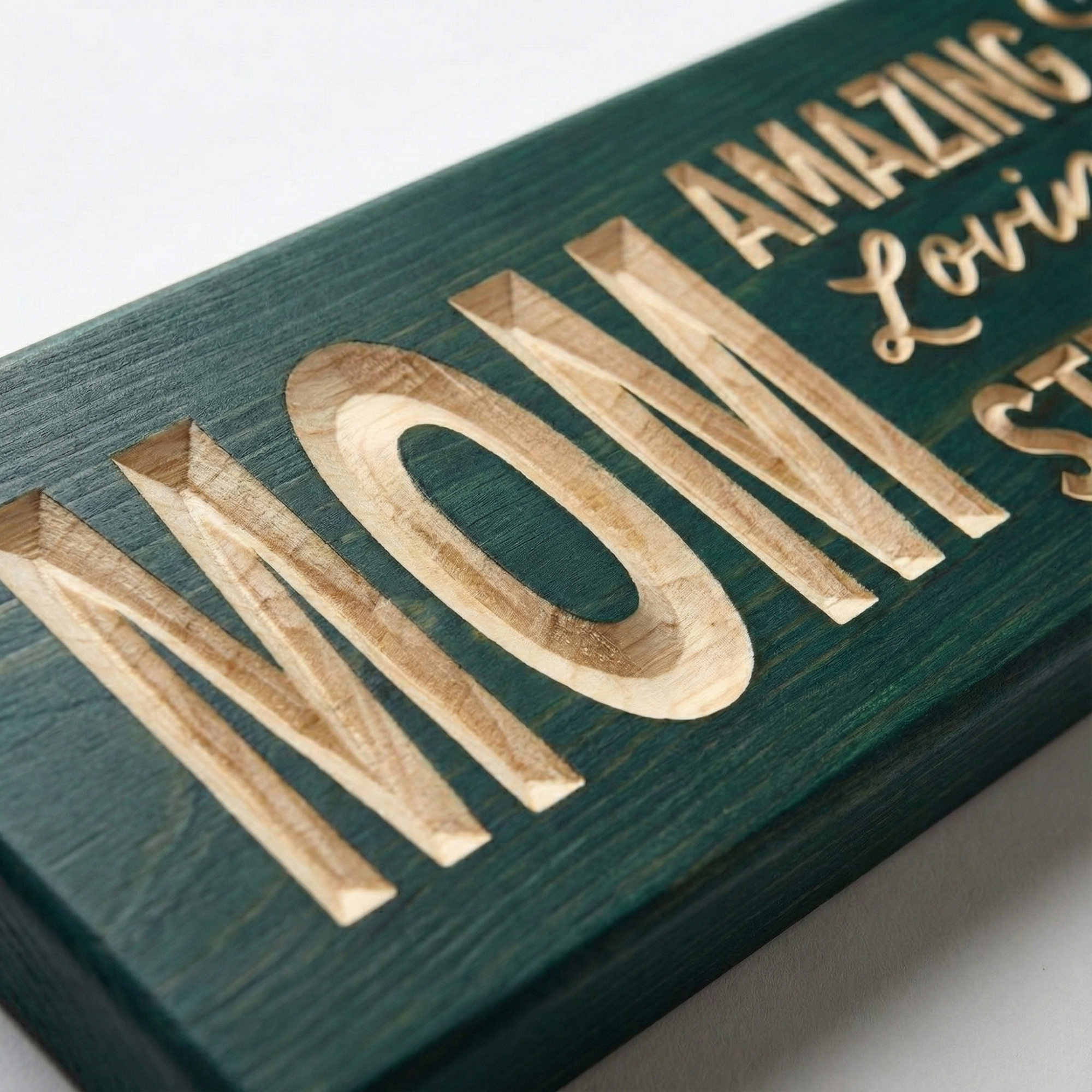 "Close-up detail of the deep CNC carving on the 'MOM' wood sign by Bluegrass Gifts, highlighting the natural wood grain texture and teal finish."