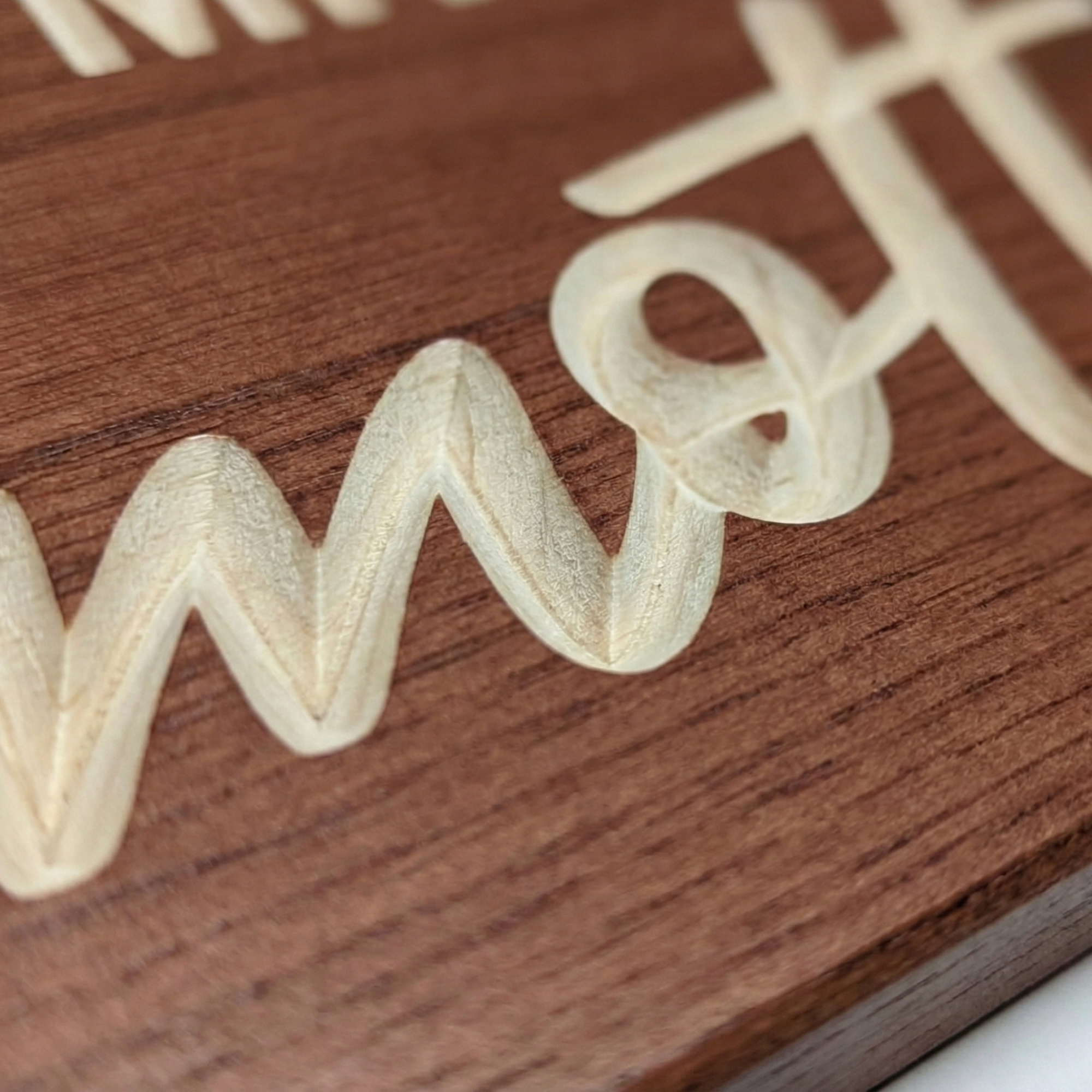Extreme close-up of a wood sign showing the physical depth and texture of CNC V-carved lettering.