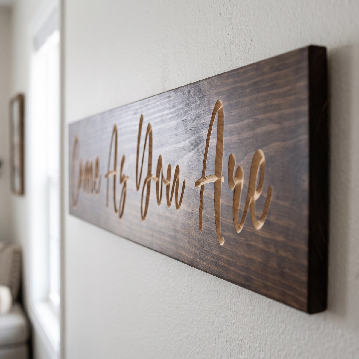 Close-up of the carved letters on the Come As You Are sign, natural pine inside the cuts against the stained grain