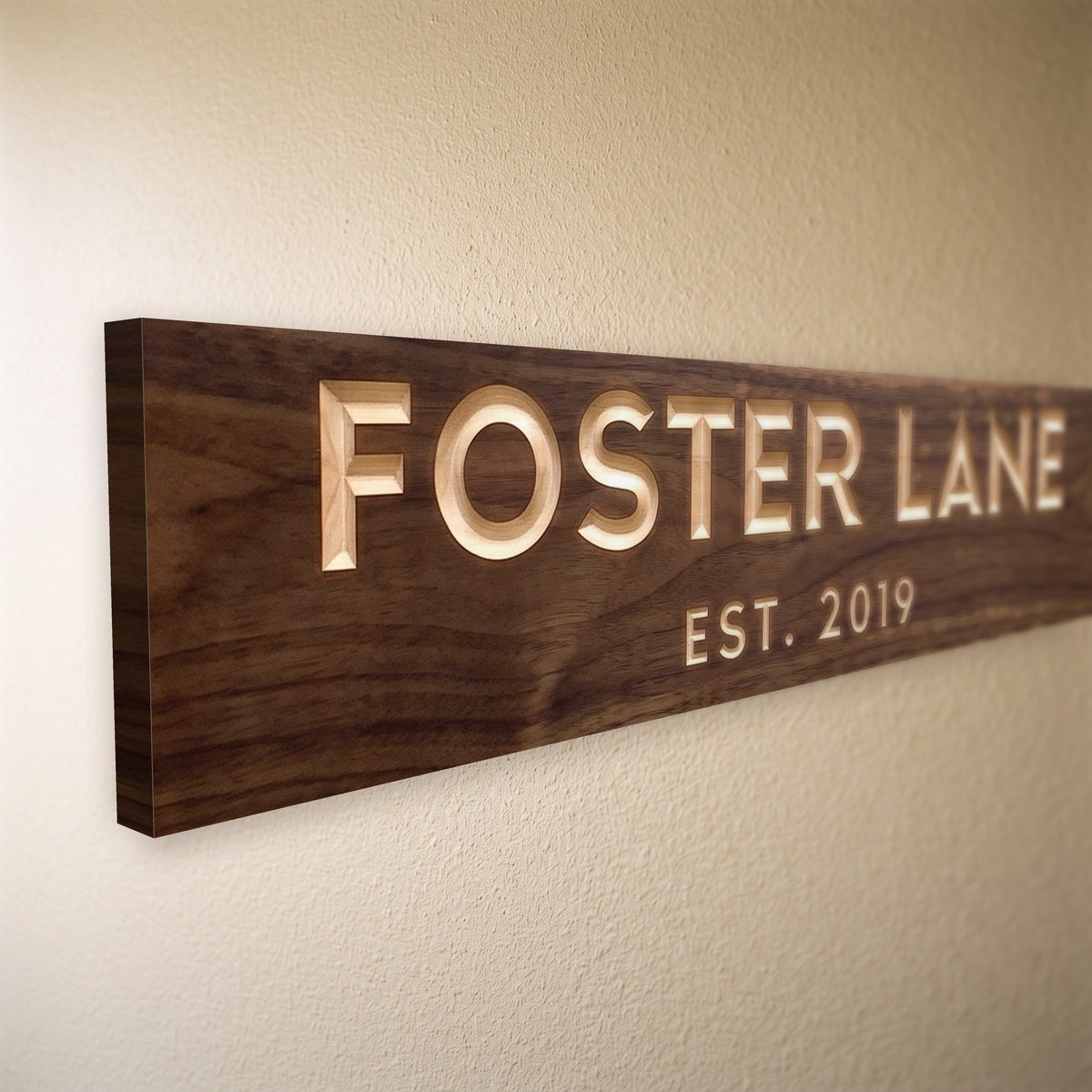 Close-up of the carved letters on the Foster Lane sign, natural pine inside the cuts against the stained grain