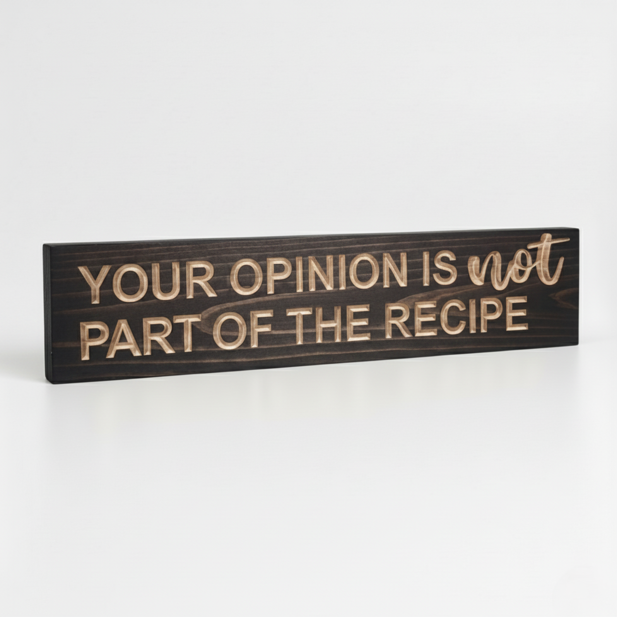 Angled view of a dark walnut stained wooden kitchen plaque showing deep CNC carved lettering and natural wood grain.