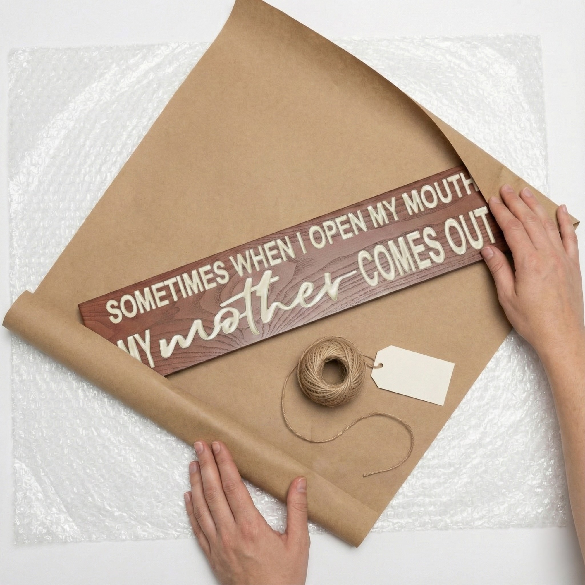 Overhead view of a funny carved wood sign being wrapped in brown craft paper with twine and a gift tag.