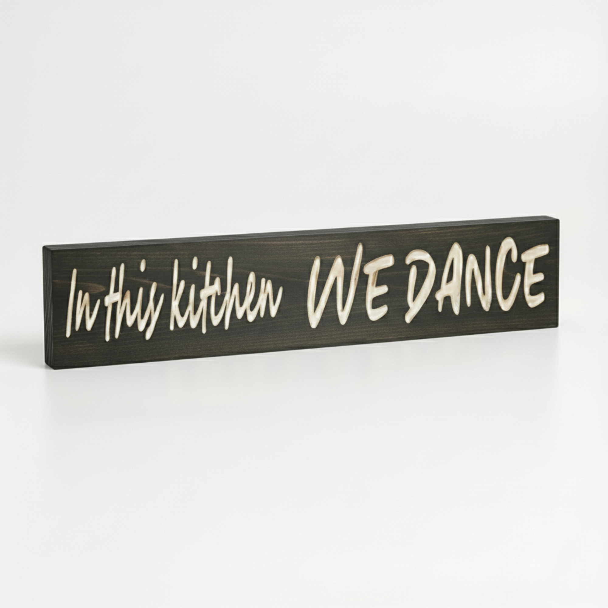 Side view of a handmade "In This Kitchen We Dance" sign showing the thickness of the solid Kentucky hardwood and the depth of the CNC carving.