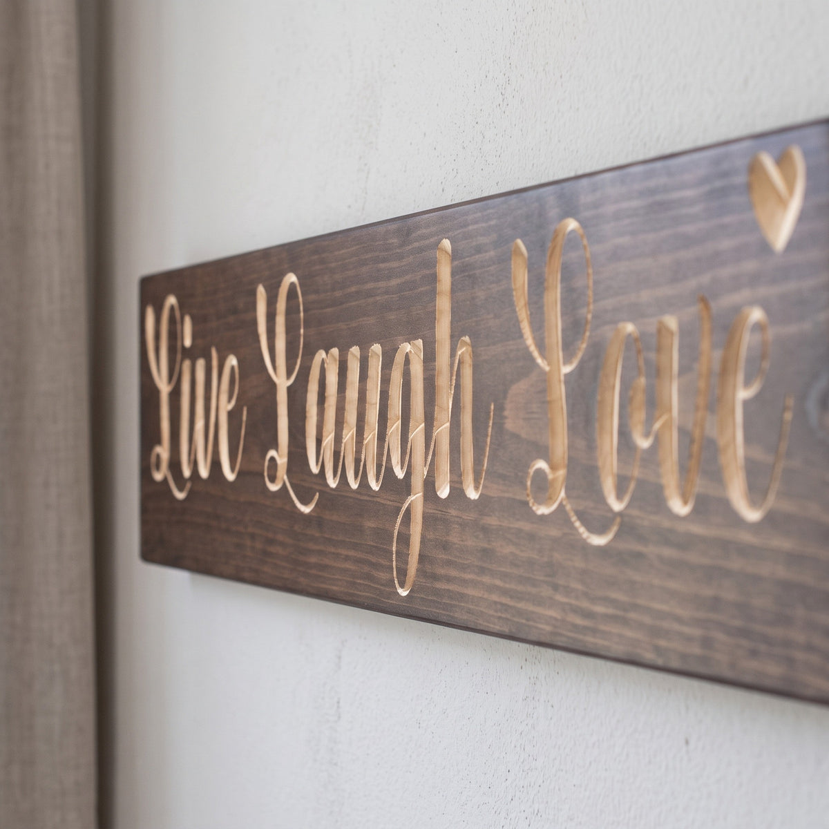 Close-up of the carved letters on the Live Laugh Love sign, natural pine inside the cuts against the stained grain
