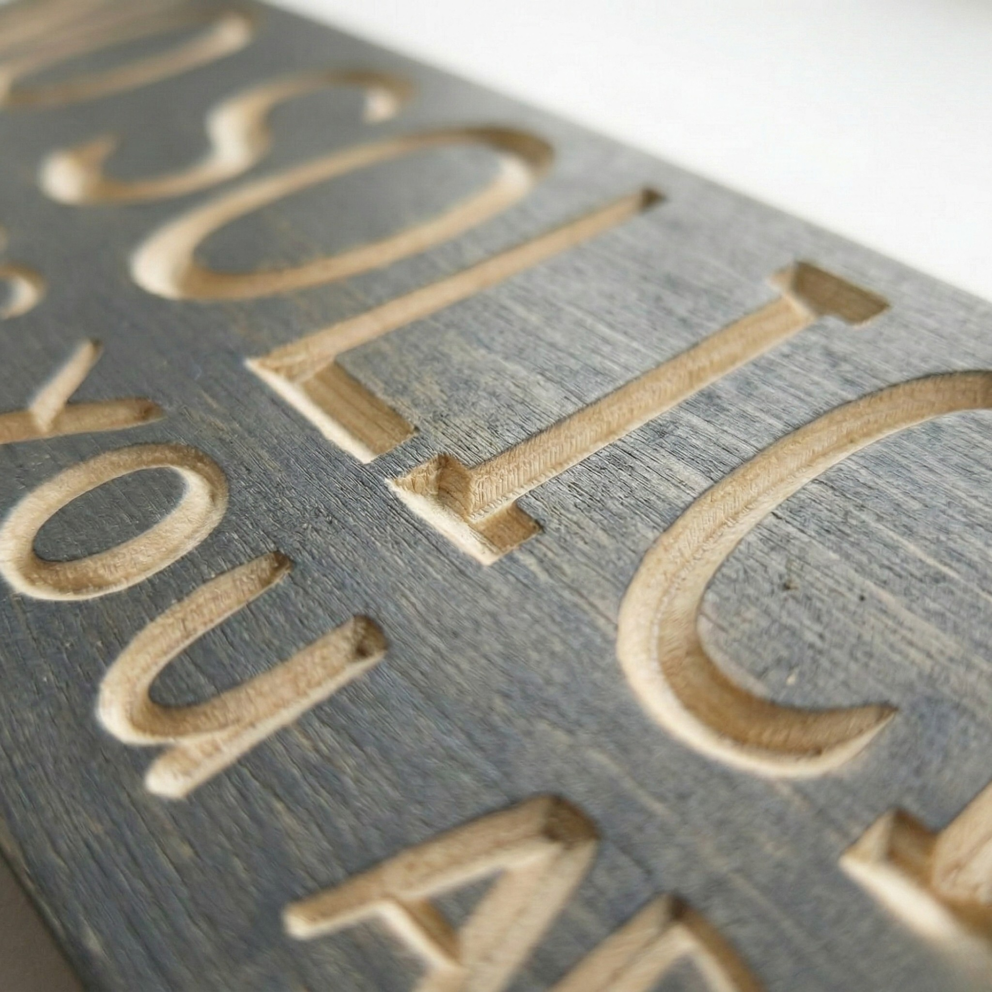 Extreme macro close-up of deep V-carved letters on a wooden sign, showing natural grain texture and high-quality craftsmanship.