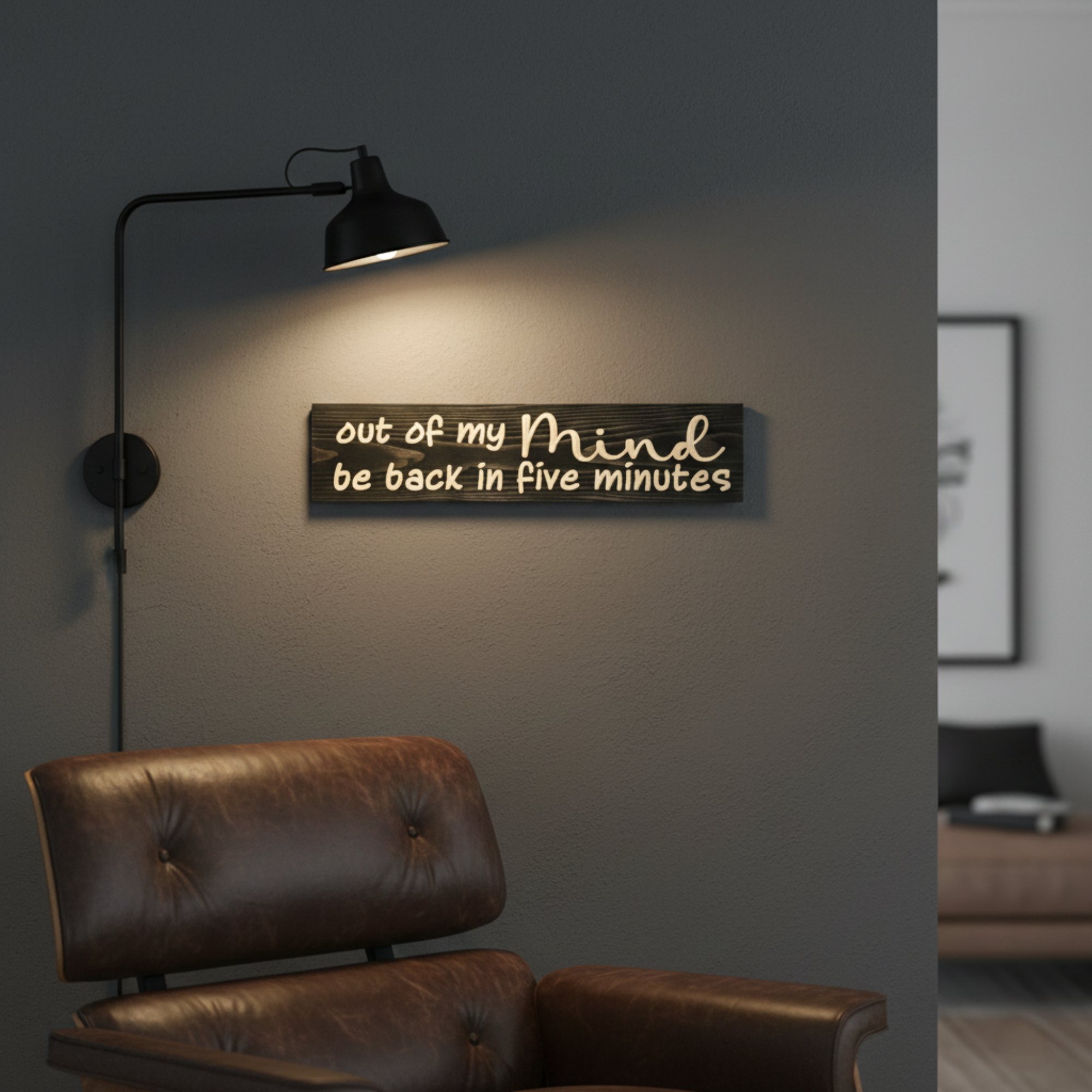 Witty wooden wall art hanging under a modern black lamp in a cozy home office or reading nook.
