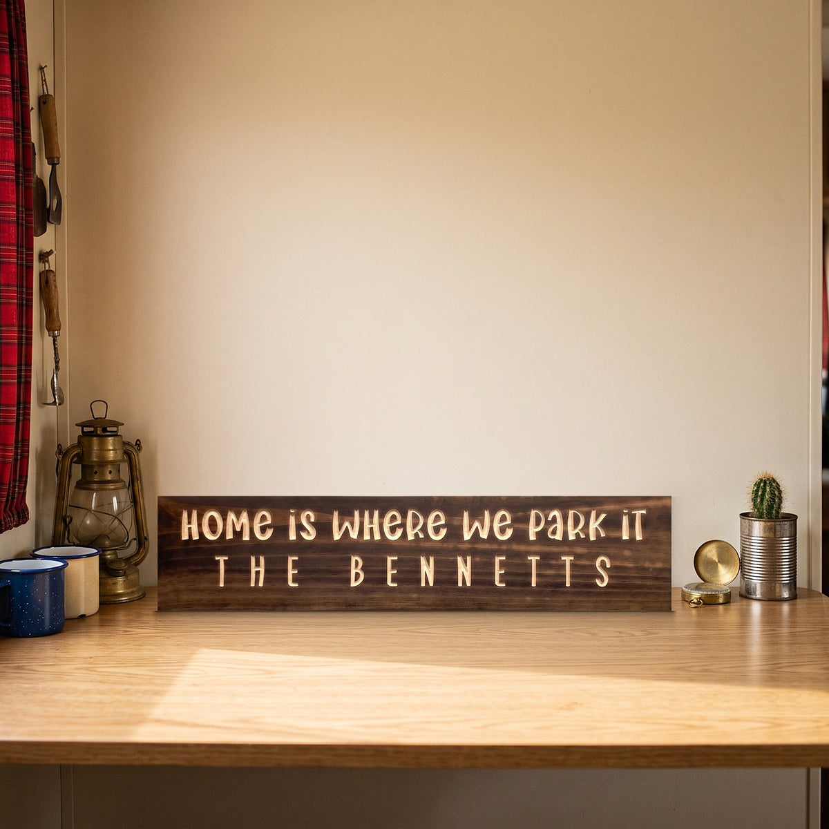 Home Is Where We Park It personalized wood sign standing on an RV dinette table beside a lantern, enamel mugs and a small cactus