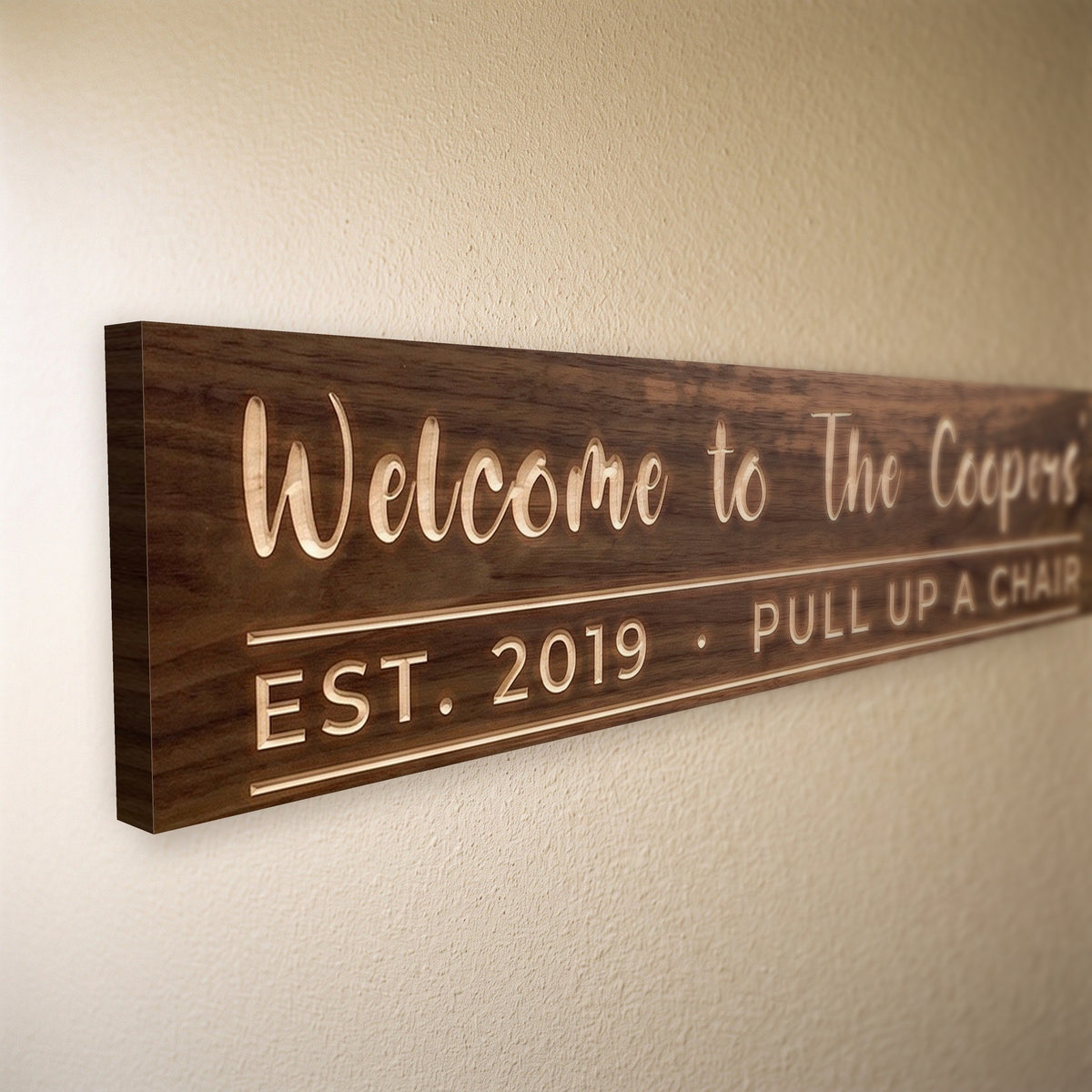 Close-up of the carved letters on the Welcome to The Coopers' sign, natural pine inside the cuts against the stained grain