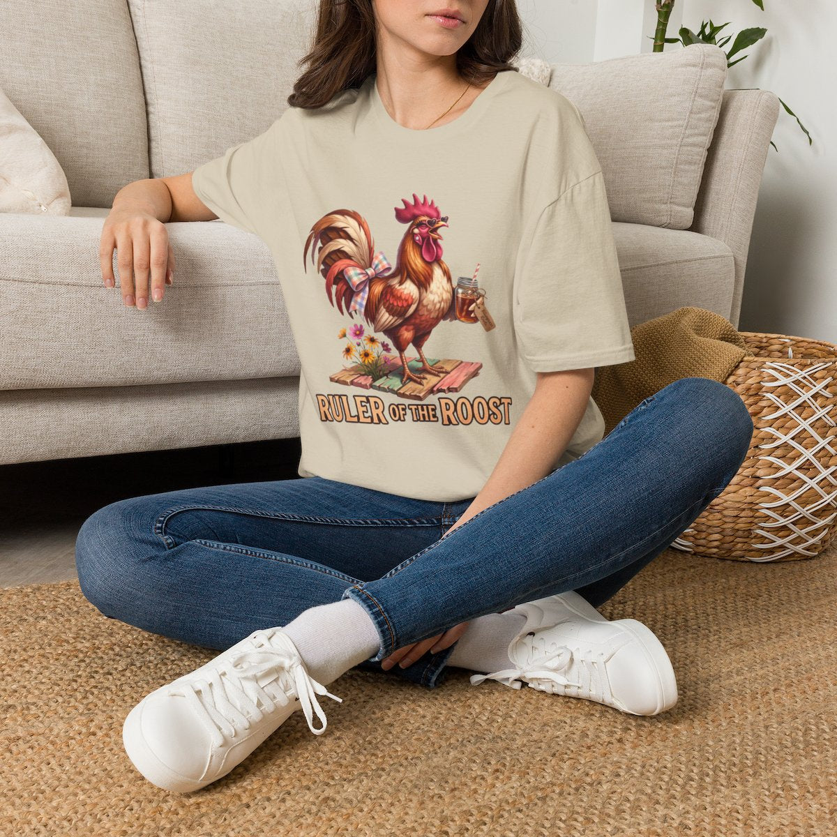 A woman sitting cross-legged on a rug, wearing a beige Rooster Shirt - Ruler of the Roost, in a relaxed pose