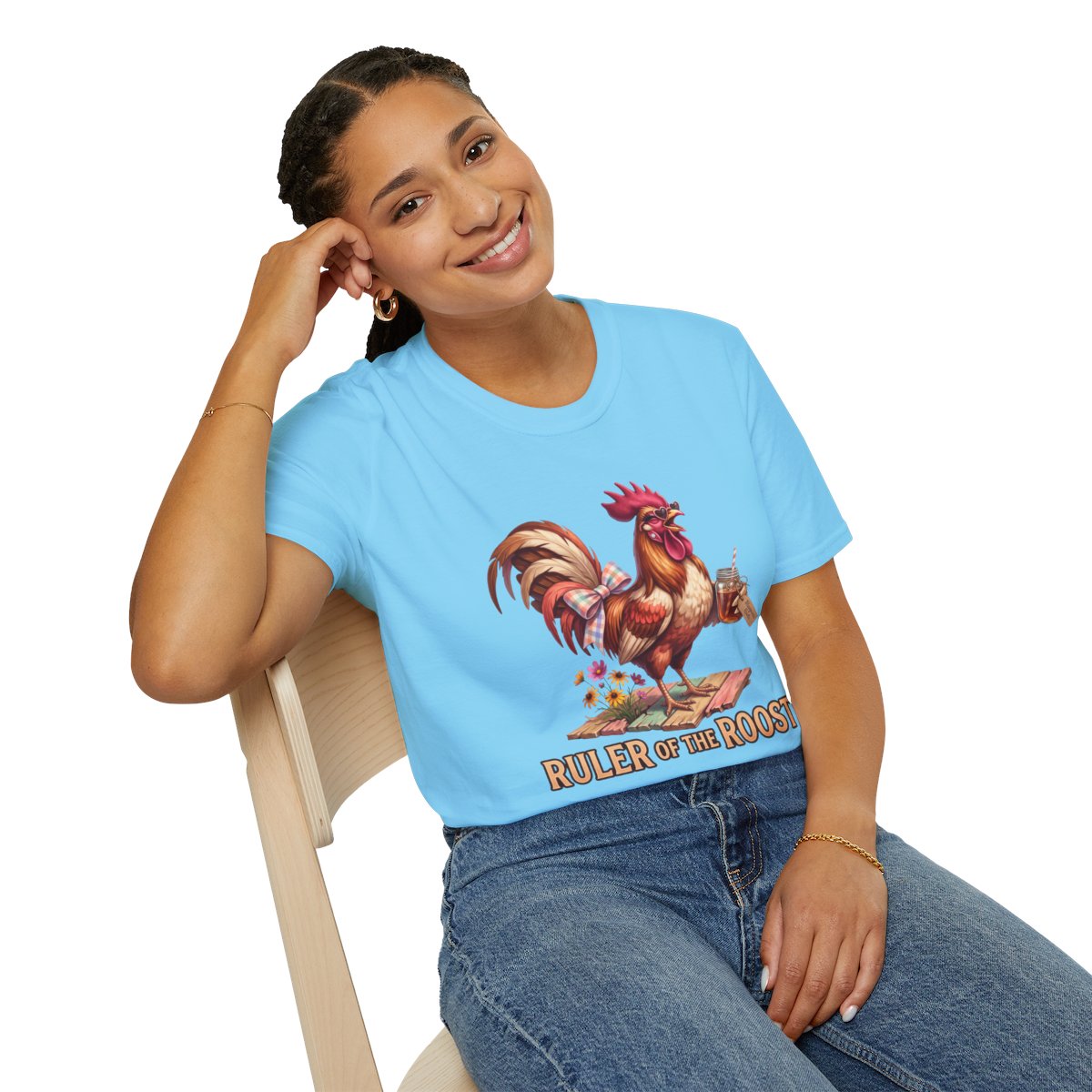 A woman sits casually, smiling, wearing the light blue "Rooster Shirt - Ruler of the Roost" with a relaxed fit