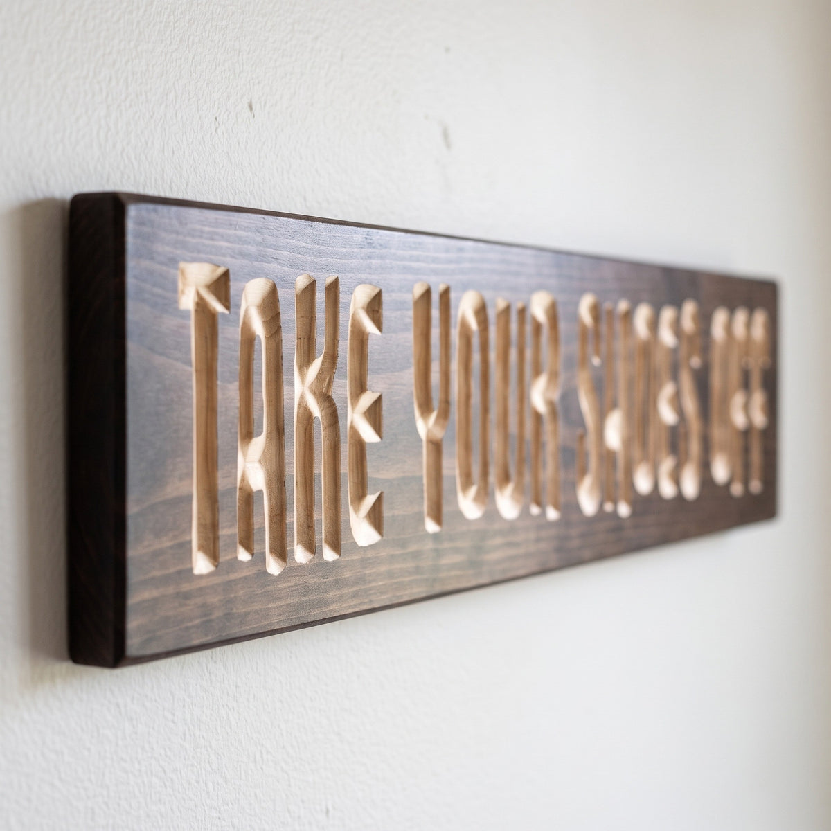 Close-up of the carved letters on the Take Your Shoes Off sign, natural pine inside the cuts against the stained grain