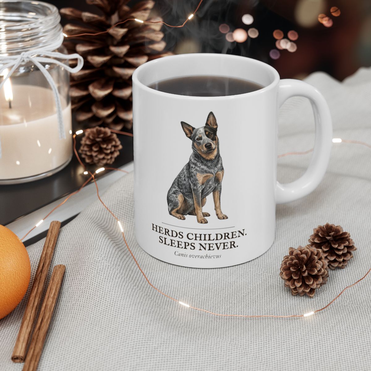 A Dog Mom Mug filled with a dark beverage sits on a festive table with pinecones, a candle, and string lights
