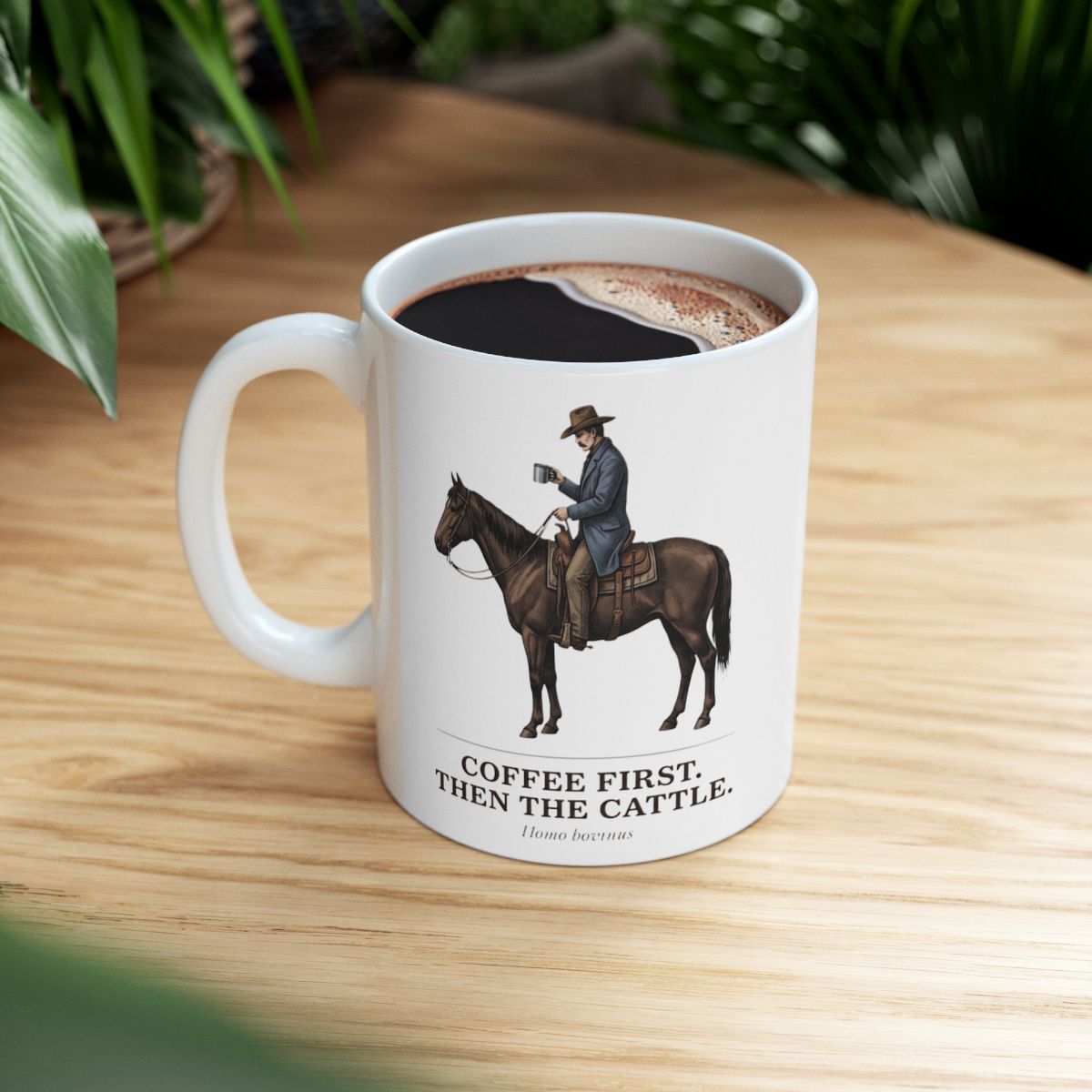 A top-down view of the Cowboy Coffee Mug, filled with coffee, on a wooden table with lush green plants in the background
