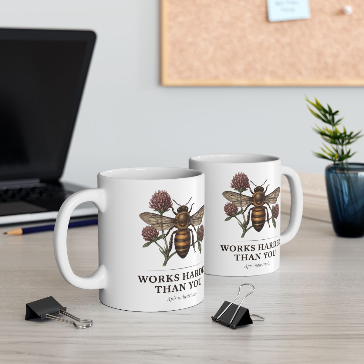 Two white Bee Coffee Mugs on a desk, one in front of a laptop, with office supplies and a plant in the background