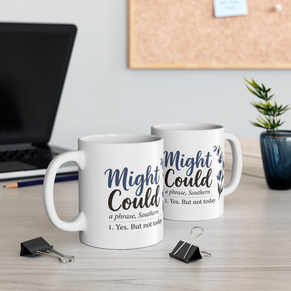 Two white Mug With Sayings are displayed on a desk, one in front of the other, near a laptop and office supplies