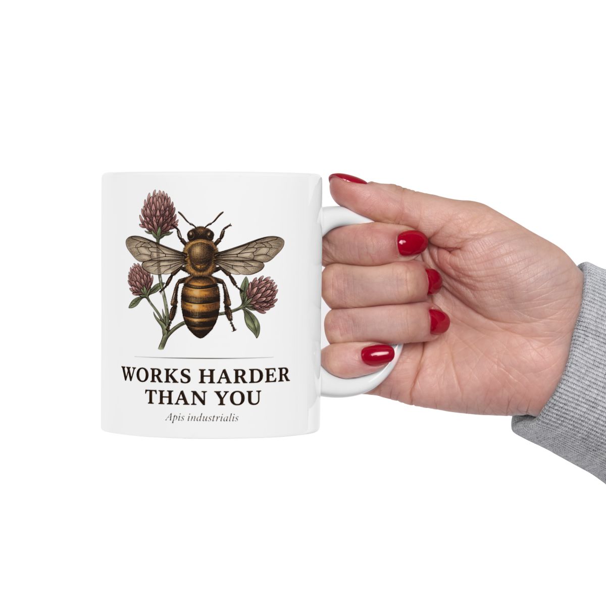 A hand with bright red painted nails holding the white Bee Coffee Mug by its handle, presented against a plain white background