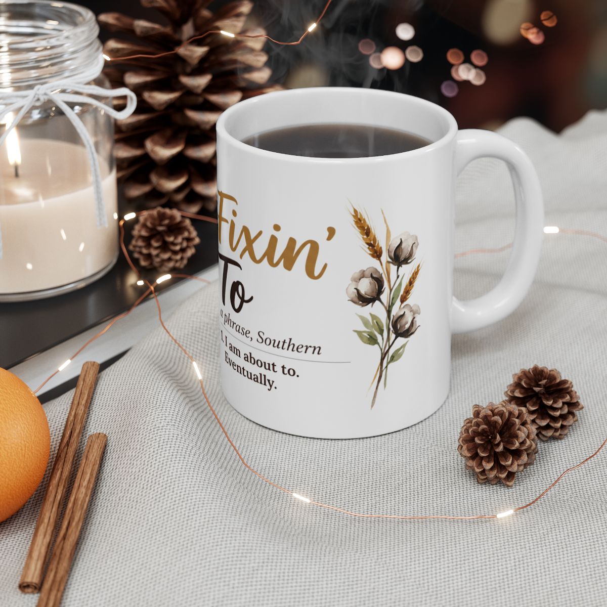 A white ceramic Definition Mug with coffee, surrounded by pinecones, fairy lights, and a candle in a cozy setting