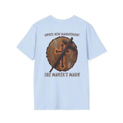 Light blue premium t-shirt featuring a high-resolution back-print of a natural timber log round with detailed growth rings. Centered on the wood grain is a glowing, ember-lit cross that appears deeply scorched into the surface, emitting light wisps of white smoke. A rustic, weathered metal branding iron in the shape of a cross leans diagonally against the wood.

The arched text above the graphic reads "UNDER NEW MANAGEMENT" in a distressed orange, vintage-style font. Below the timber round, the bold text re