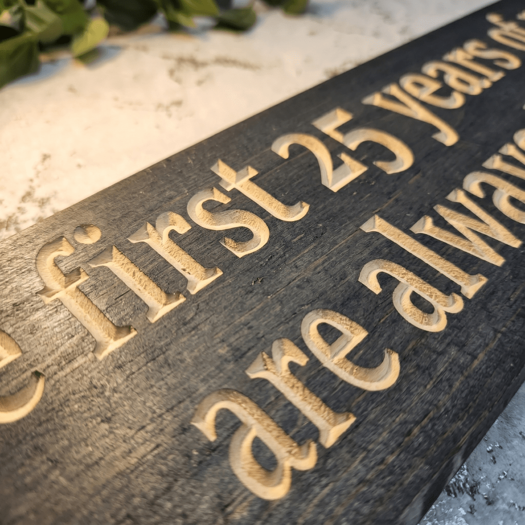 Macro close-up of CNC-carved lettering on 25th anniversary wood sign showing deep relief carving and natural wood grain contrast in dark stain