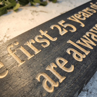 Macro close-up of CNC-carved lettering on 25th anniversary wood sign showing deep relief carving and natural wood grain contrast in dark stain