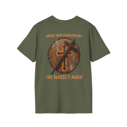 Green premium t-shirt featuring a high-resolution back-print of a natural timber log round with detailed growth rings. Centered on the wood grain is a glowing, ember-lit cross that appears deeply scorched into the surface, emitting light wisps of white smoke. A rustic, weathered metal branding iron in the shape of a cross leans diagonally against the wood.

The arched text above the graphic reads "UNDER NEW MANAGEMENT" in a distressed orange, vintage-style font. Below the timber round, the bold text reads "
