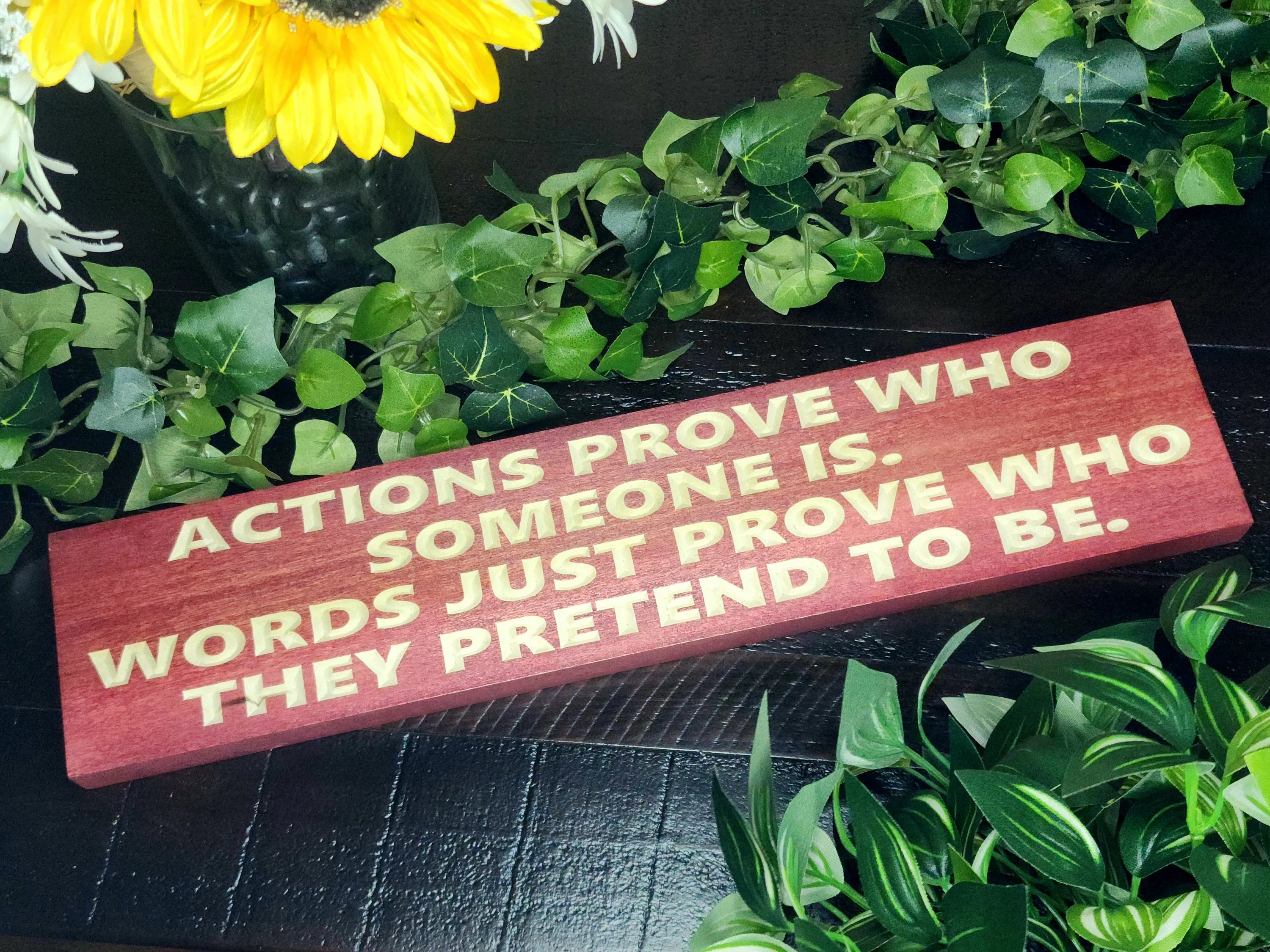 "Actions Prove Who Someone Is" motivational wood sign displayed in a modern office space.
