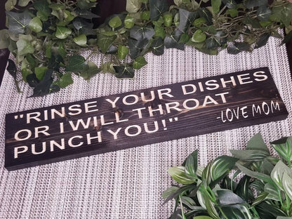 Funny kitchen wall sign reading "Rinse Your Dishes or I Will Throat Punch You, Love Mom" displayed near a sink.
