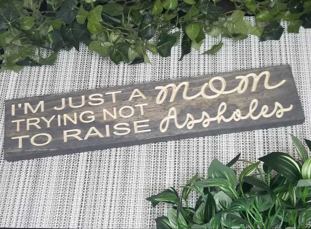 I’m Just a MOM Trying Not to Raise Assholes wood sign for parenting humor and home decor.
