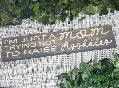 I’m Just a MOM Trying Not to Raise Assholes wood sign for parenting humor and home decor.

