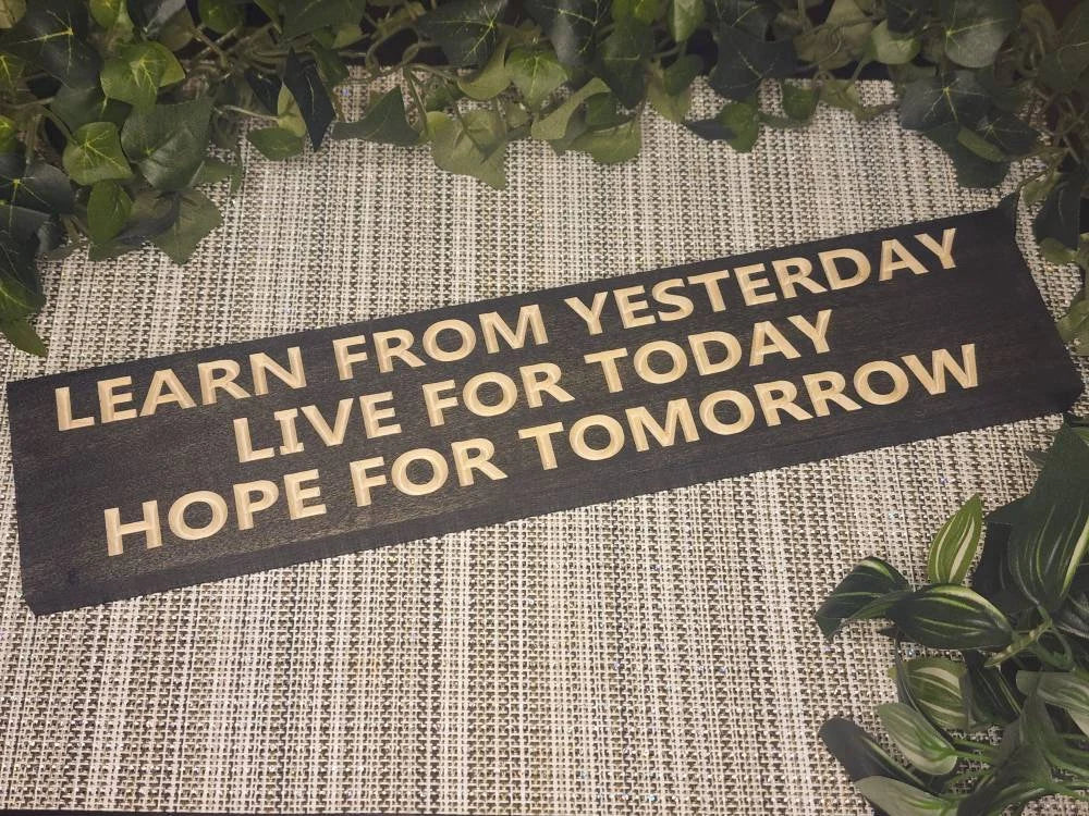 "Learn from Yesterday, Live for Today, Hope for Tomorrow" wooden sign displayed in a cozy, serene meditation space.
