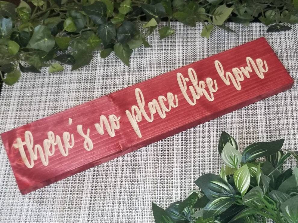 Rustic "There's No Place Like Home" wooden sign displayed in a cozy farmhouse living room.
