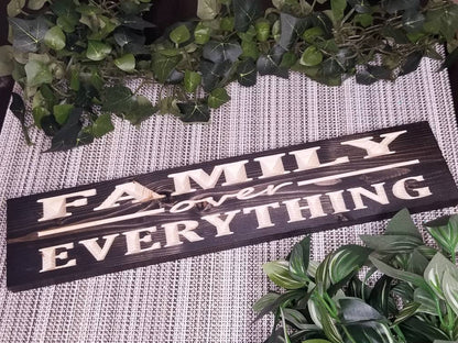 Rustic wooden Family Over Everything wall art displayed in a cozy living room.
