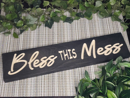 Rustic wooden sign reading Bless This Mess displayed in a cozy farmhouse living room.
