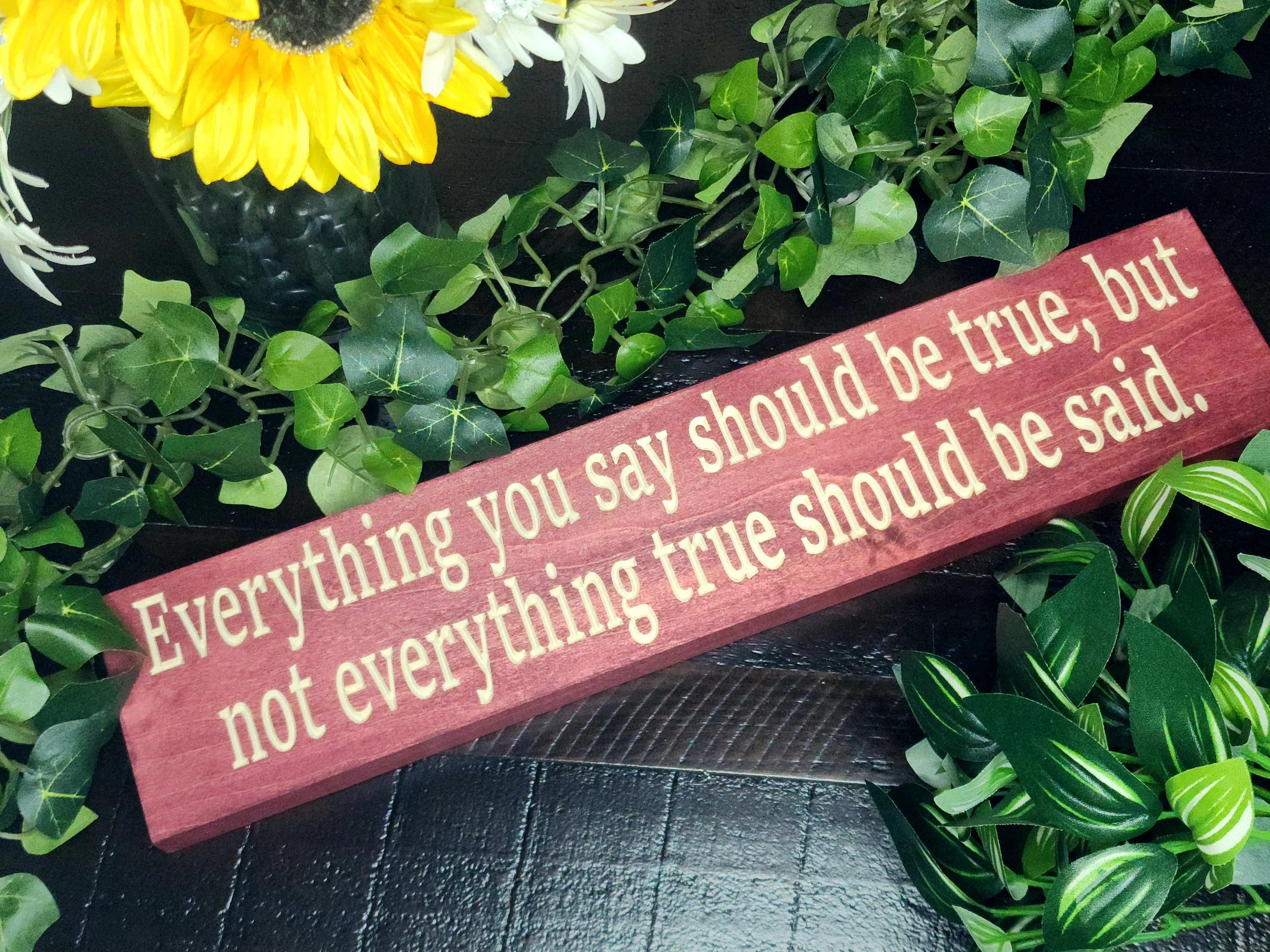 Rustic wooden sign reading Everything You Say Should Be True, But Not Everything True Should Be Said displayed in a cozy home office.
