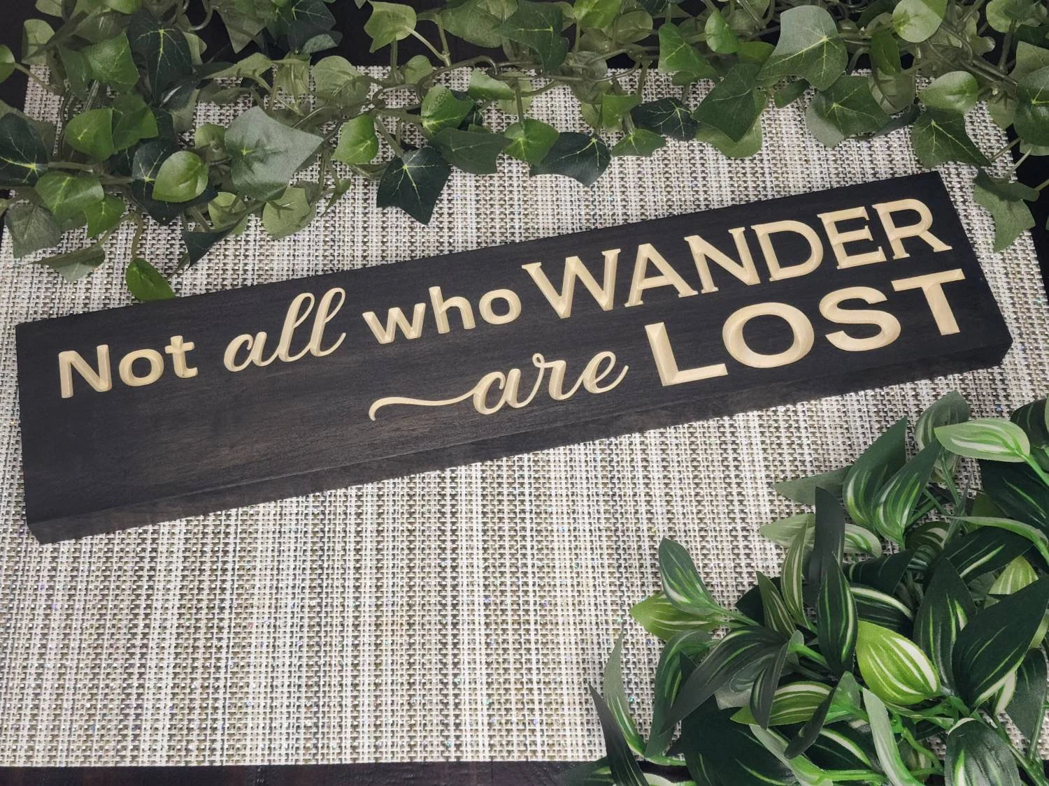 Rustic wooden sign reading "Not All Who Wander Are Lost" displayed in an adventure-themed living room.
