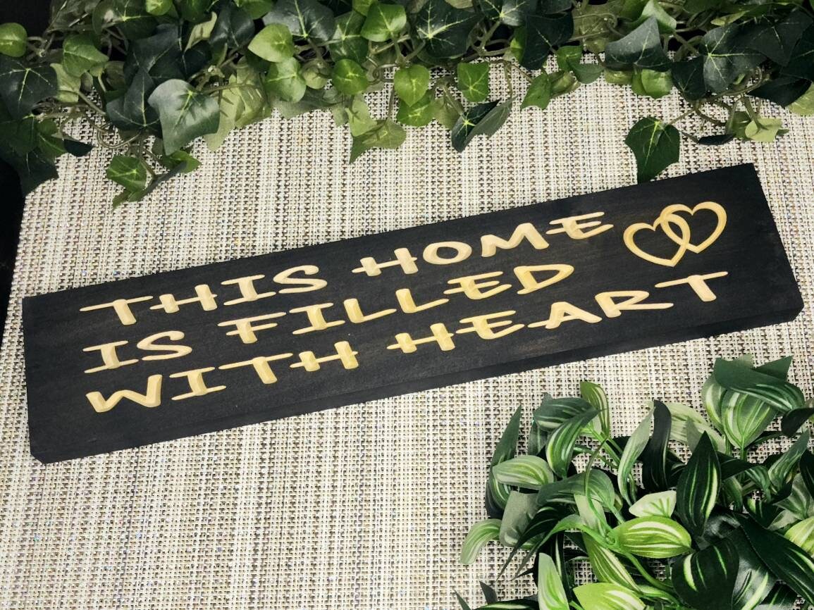 Rustic wooden sign reading This Home is Filled with Heart displayed on a cozy living room wall.
