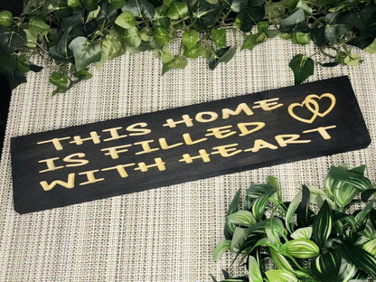 Rustic wooden sign reading This Home is Filled with Heart displayed on a cozy living room wall.