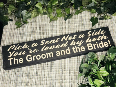Rustic wooden wedding seating sign reading Pick a Seat, Not a Side, You're Loved by Both the Groom and the Bride.
