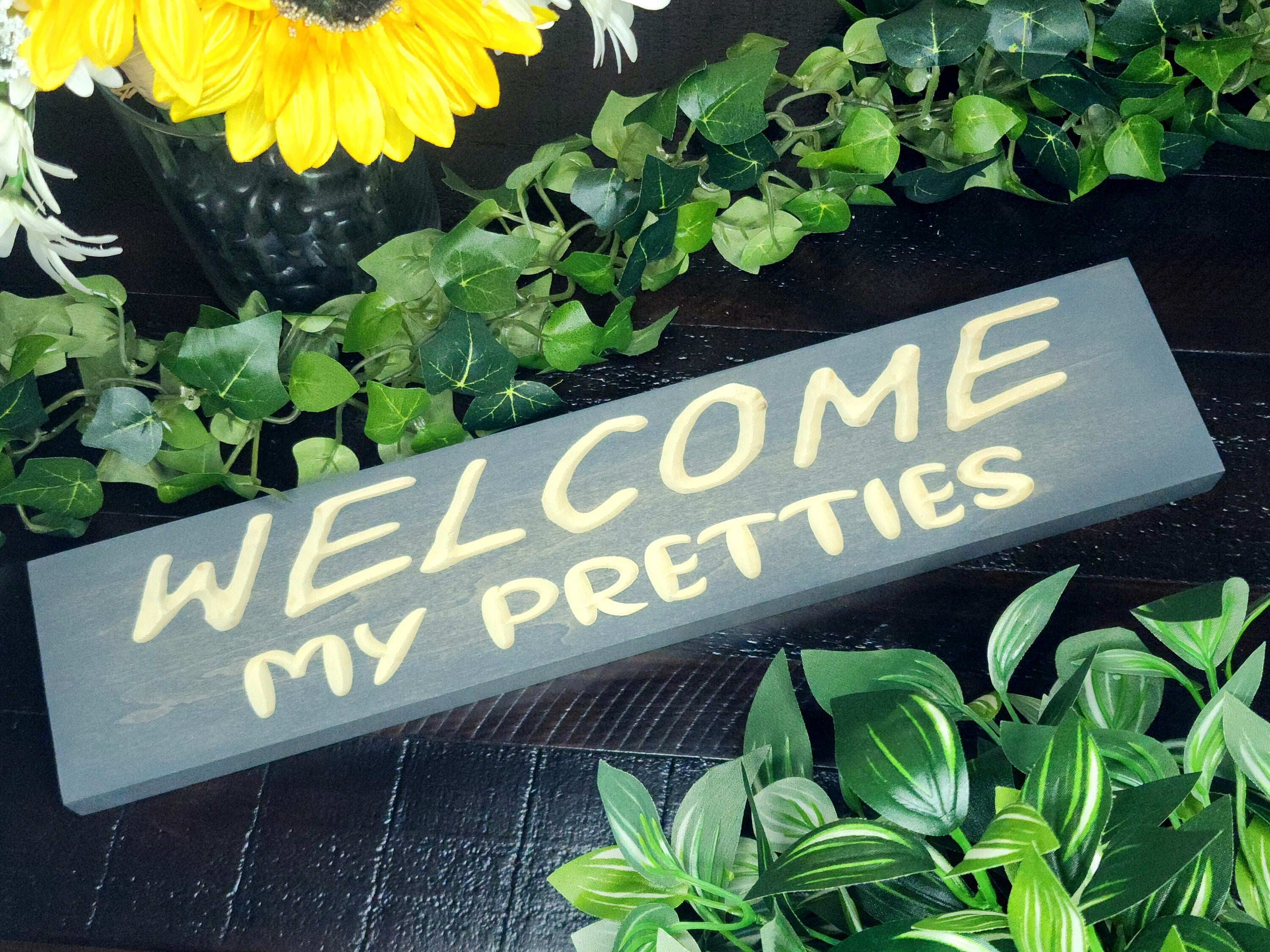"Welcome My Pretties" wooden Halloween sign displayed on a festive porch.
